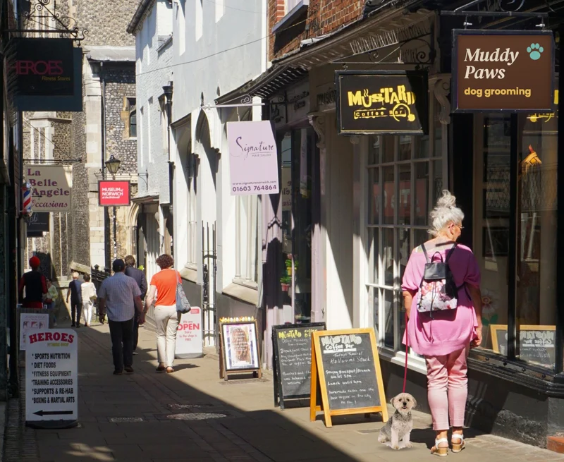 A shopper in a pink top, with her small dog on a lead, outside the Muddy Paws dog grooming shop