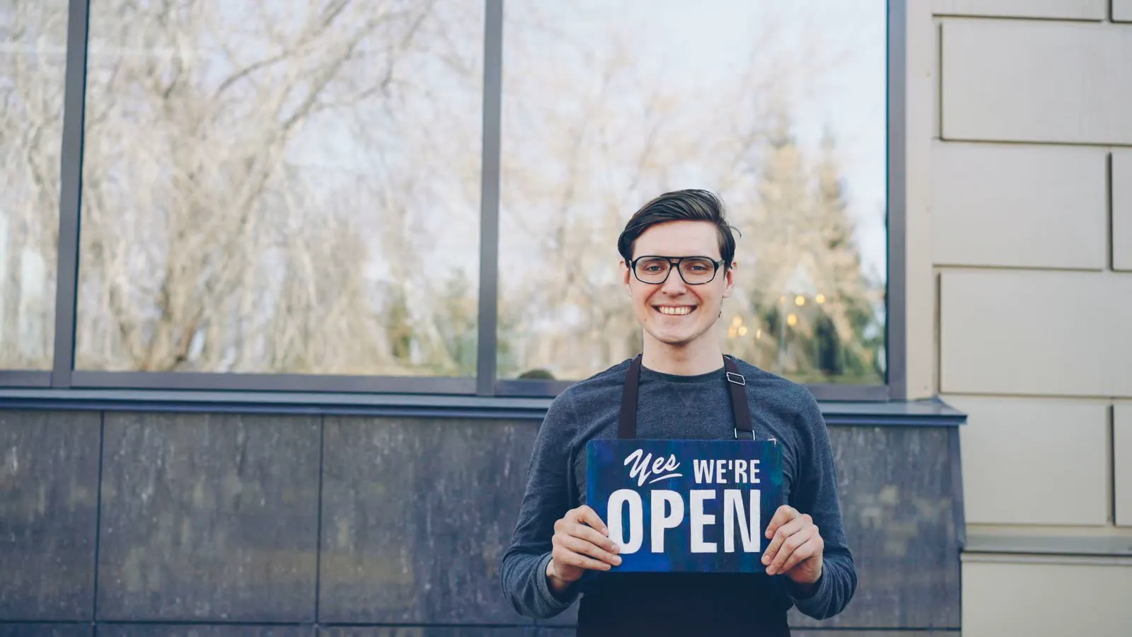 A smiling shop owner holding a Yes, we’re open sign