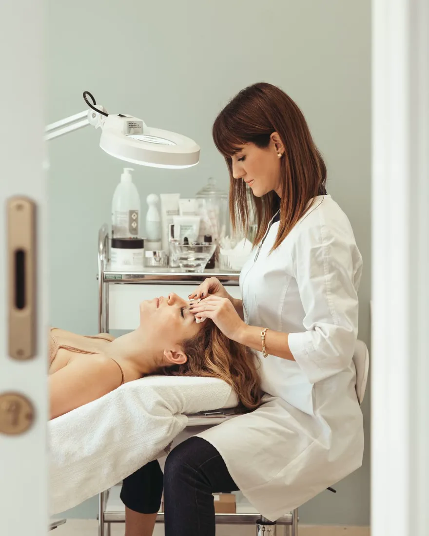 An aesthetician giving a calm facial treatment in a softly lit clinic